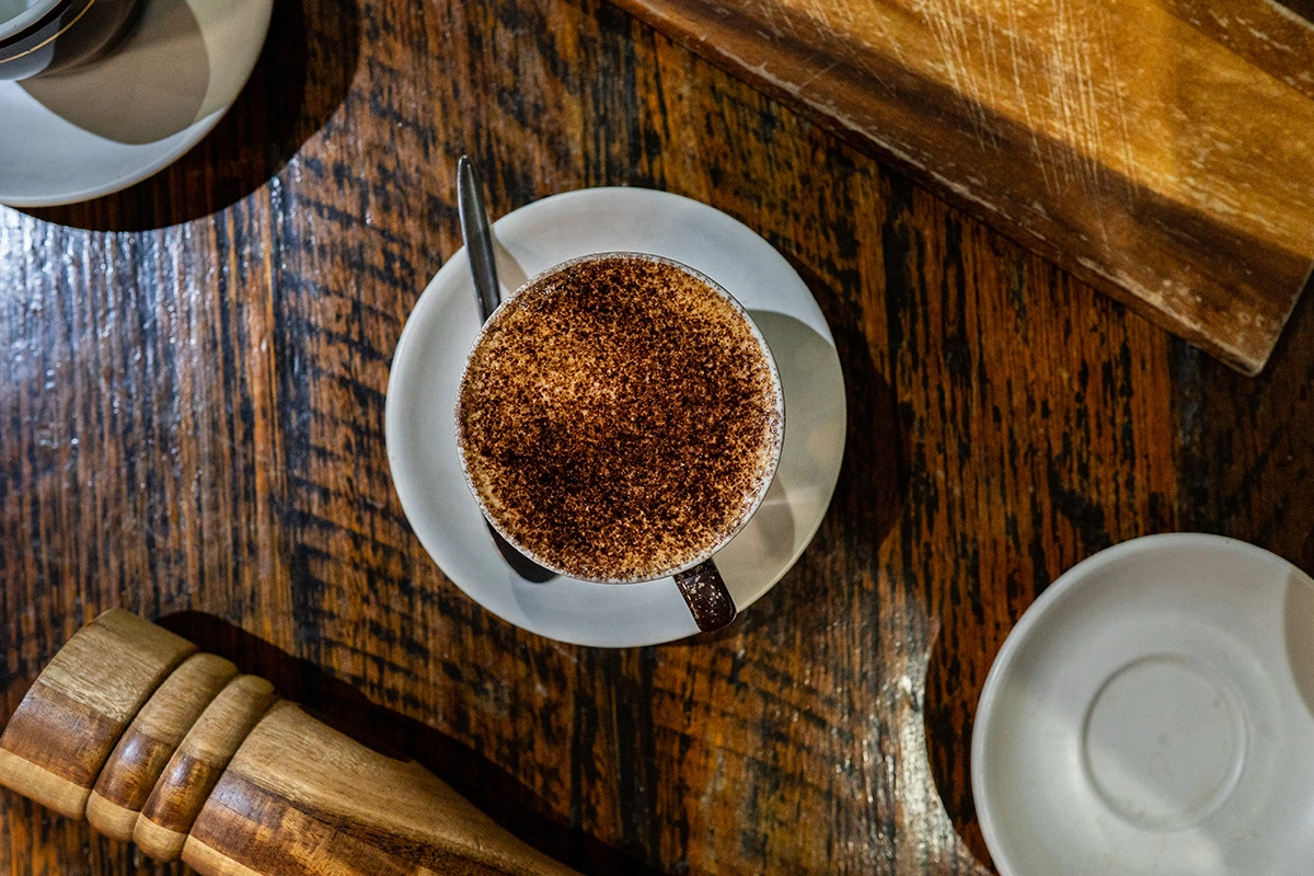 Cappuccino dusted with cocoa on a saucer, top-down on a wooden table